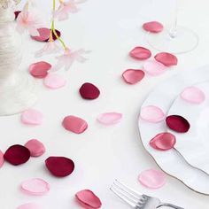 the table is set with pink and white plates, silverware and confetti