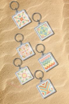 six keychains with different designs on them sitting in the sand