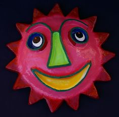 a painted sun face with big eyes and a smile on it's face, against a black background