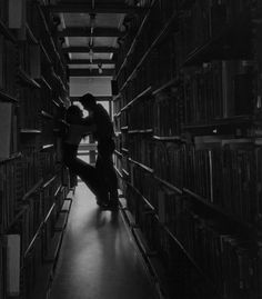 black and white photograph of two people kissing in the middle of a library filled with books