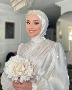 a woman in a white dress holding a flower and smiling at the camera while wearing a headscarf