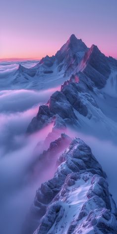 the top of a mountain covered in snow and clouds at sunset with pink hues