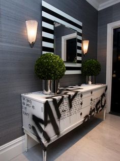 a white dresser with black and white stripes painted on the side by two potted plants