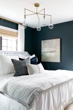 a bedroom with blue walls, white bedding and chandelier hanging from the ceiling