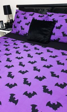 a bed covered in purple and black bat print sheets with two pillows on each side