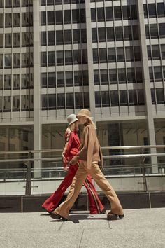 two people walking down the street in front of tall buildings