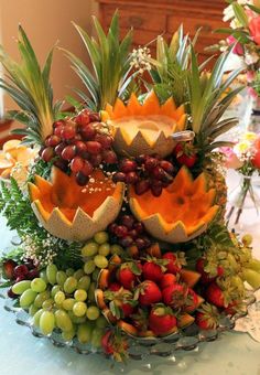 an arrangement of fruit is displayed on a table with flowers and greenery in the background