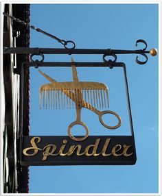 a sign for a hair salon with scissors and combs hanging from it's side