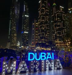 the words dubai marina are lit up in front of some tall buildings and skyscrapers