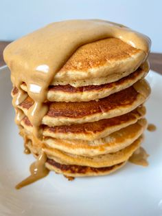 stack of pancakes covered in syrup on top of a white plate with caramel drizzle