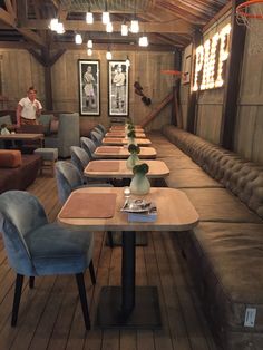 a restaurant with wooden tables and blue chairs in the center, while a man stands at the far end of the room