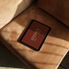 an electronic device sitting on top of a brown chair next to a tan pillow with the word joy written on it