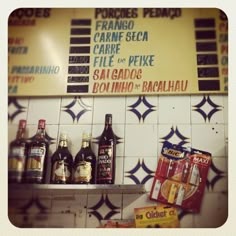 several bottles of alcohol are on the shelf in front of a restaurant sign and tiled wall