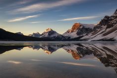 the mountains are reflected in the still water on the lake's surface as the sun sets