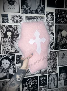 someone is holding up a pink pillow with a white cross on it in front of black and white wallpaper