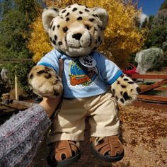 a stuffed animal that is holding onto a fence post with trees in the back ground