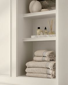 towels stacked on top of each other in a white shelf next to bottles and vases