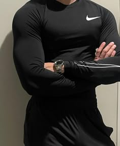 a man with his arms crossed standing in front of a wall wearing a nike shirt