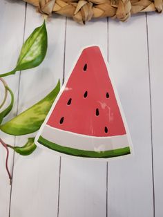 a piece of watermelon sitting on top of a wooden table next to a plant