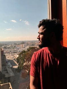 a man standing in front of a window looking out at the city