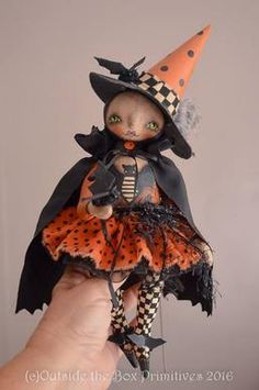 a hand holding a doll wearing a witch costume