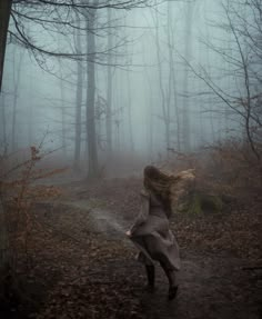 a woman is running through the woods on a foggy day with her hair blowing in the wind