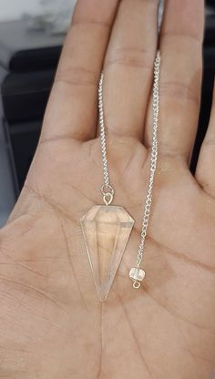 a person's hand is holding a clear crystal pendant on a chain that hangs from the middle of their palm