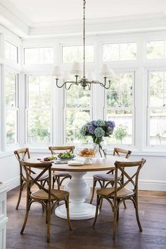 a dining room table with chairs around it and flowers in vases on the table