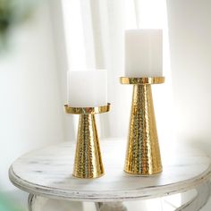 two gold and white candles sitting on top of a table