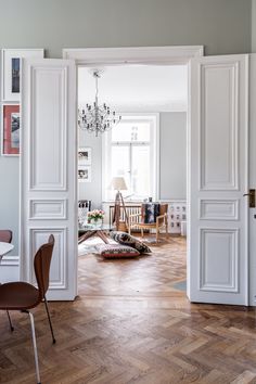 an open door leading into a living room with wooden floors and white walls, chandelier hanging from the ceiling