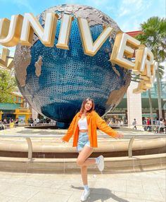 a woman posing in front of the universal studios sign with her arms out and legs crossed