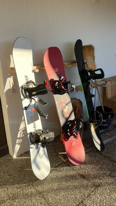 three snowboards leaning up against a wall in a room with other snowboard on the floor