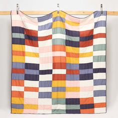 a multicolored quilt hanging on a clothes line with pegs in front of it