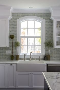 a kitchen with white cabinets and marble counter tops, along with a window over the sink