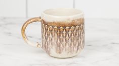 a white and brown coffee cup sitting on top of a marble counter