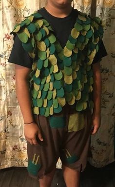 a young boy wearing a costume made out of green circles and brown shorts, standing in front of a curtain