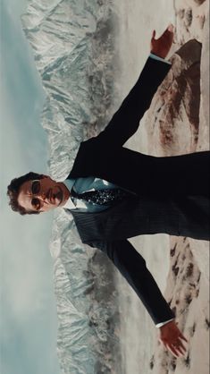 a man in a suit and tie standing next to snow covered mountains with his arms outstretched