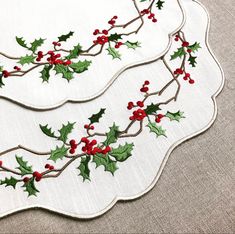 two white place mats decorated with holly and red berries