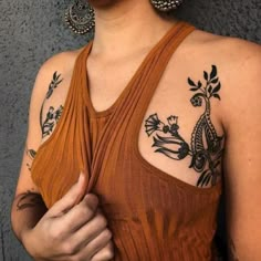 a woman with some tattoos on her chest and arm is holding something in her hand