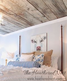 a bedroom with a cow painting on the wall next to a white bed and wooden headboard