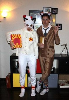 two men dressed in costumes standing next to each other on a wooden floor, one holding a bottle and the other wearing a costume