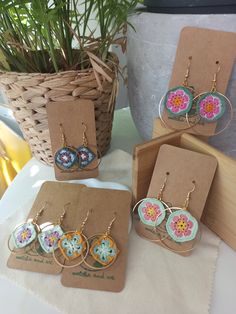 four pairs of earrings are on display in front of a basket with plants and potted plant