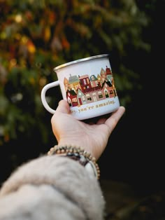 a person holding a coffee cup with houses painted on the side and writing, you're amazing