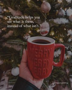 someone holding a red coffee mug in front of a christmas tree with the words, grateful helps you see what is there instead of what isn't