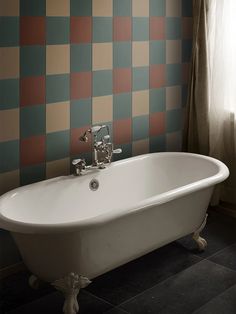 a bathtub sitting in front of a window next to a wall with checkered walls