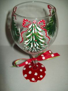 a wine glass with a christmas tree painted on the side and red polka dot ribbon