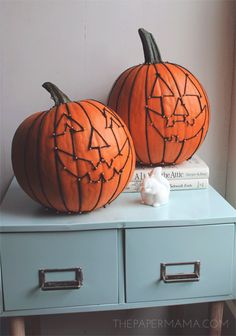 two carved pumpkins sitting on top of a blue dresser next to each other with faces drawn on them