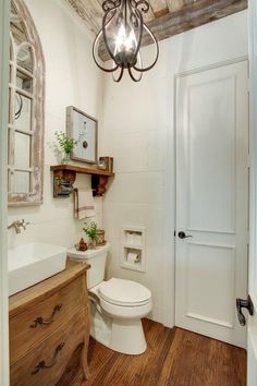 a white toilet sitting in a bathroom next to a wooden cabinet and sink under a light fixture