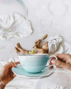 a person holding a cup and saucer with soap bubbles floating around it on a bed