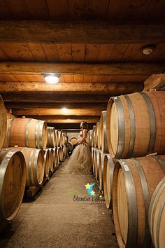 a woman in a wedding dress standing among wine barrels